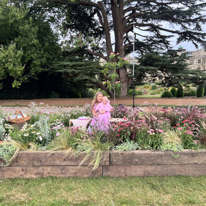 Woman holding a baby in a garden with flowers and trees