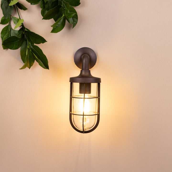 Front on image of the Agriframes Exmouth Outdoor Wall Lamp in a Bronze finish with its bulb illuminated, mounted on a neutral background. 