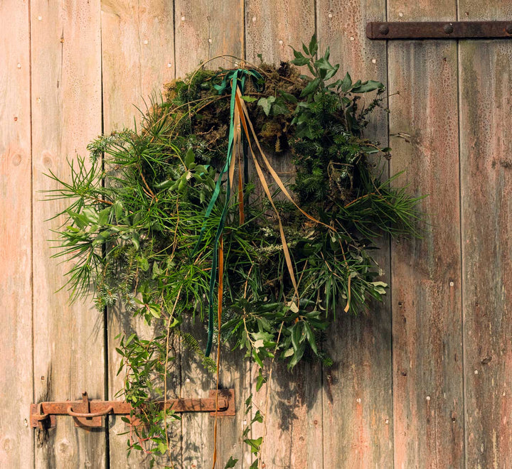 Agriframes florist wreath covered in natural materials and ribbons, mounted on a wooden door. 