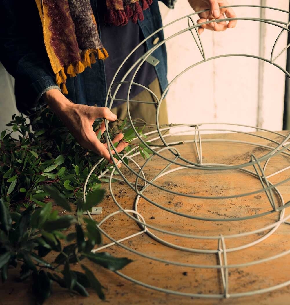 Two agriframes florist wreath trellis in a sage green finish on a wooden table, with a woman handling one of the trellis.