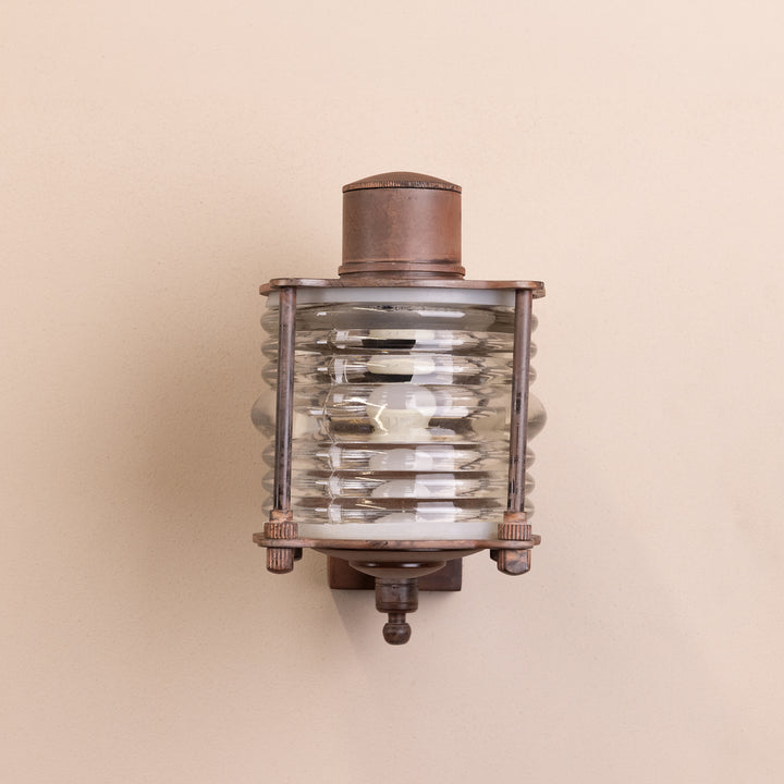 Front on image of the Agriframes Frome Outdoor Wall Lamp in a Rust-coloured finish with its bulb switched off, mounted on a neutral-coloured wall. 