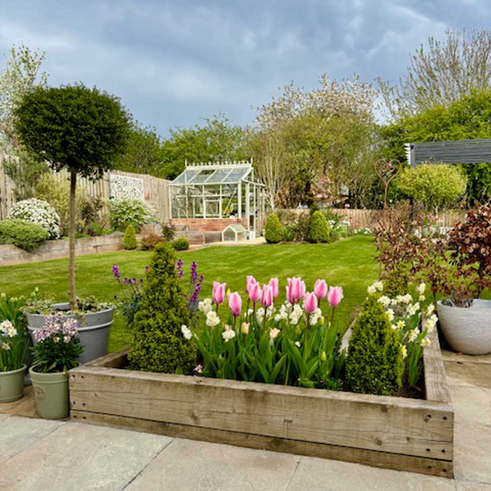 Garden scene with a wooden planter filled with flowers, including tulips, on a patio.
