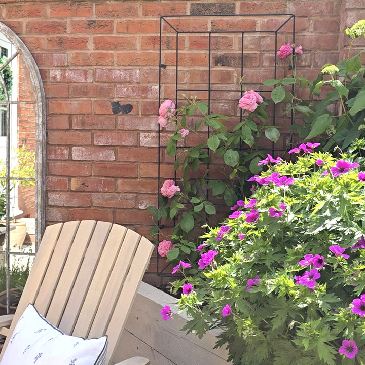 Beige chair with a pillow next to a brick wall with climbing plants and flowers.