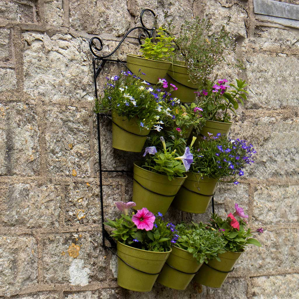 Wall-mounted plant holder with green pots and flowers against a stone wall.
