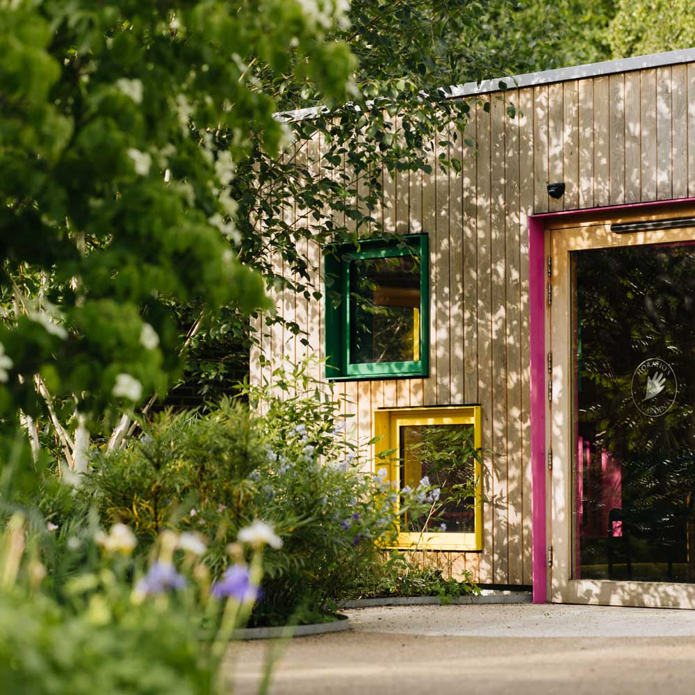 A wood panelled building within Horatio's garden, featuring multicoloured window and door frames. 