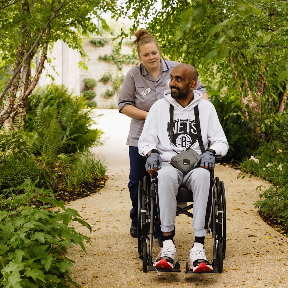 Man in a wheelchair being pushed by a woman in a garden setting