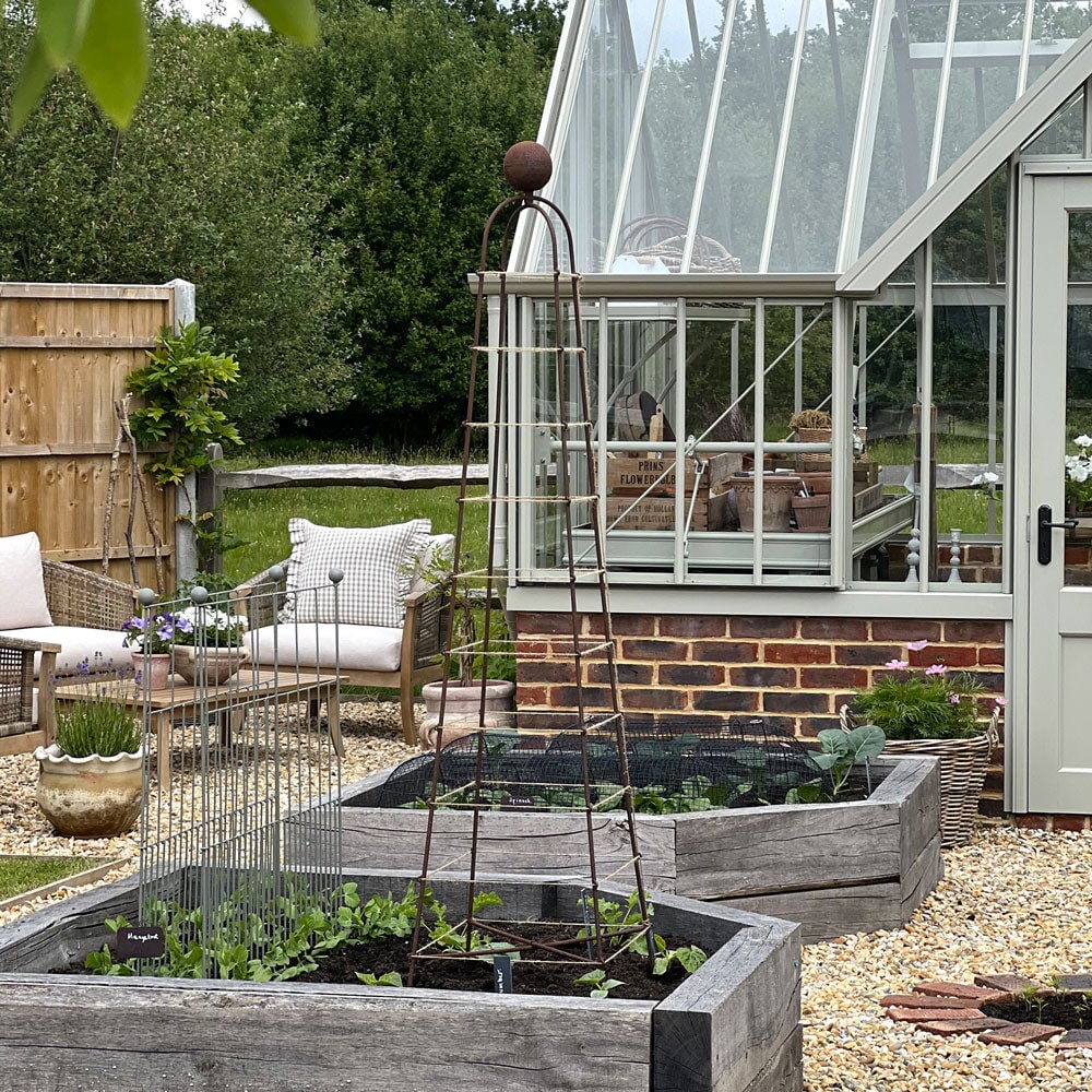 Garden scene with raised garden beds, a greenhouse, and outdoor furniture.
