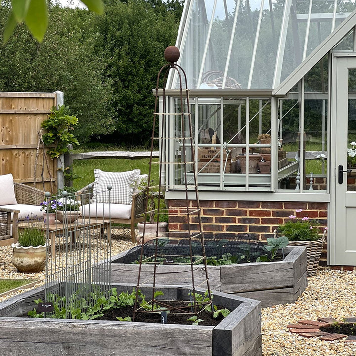 Garden scene with raised garden beds, a greenhouse, and outdoor furniture.