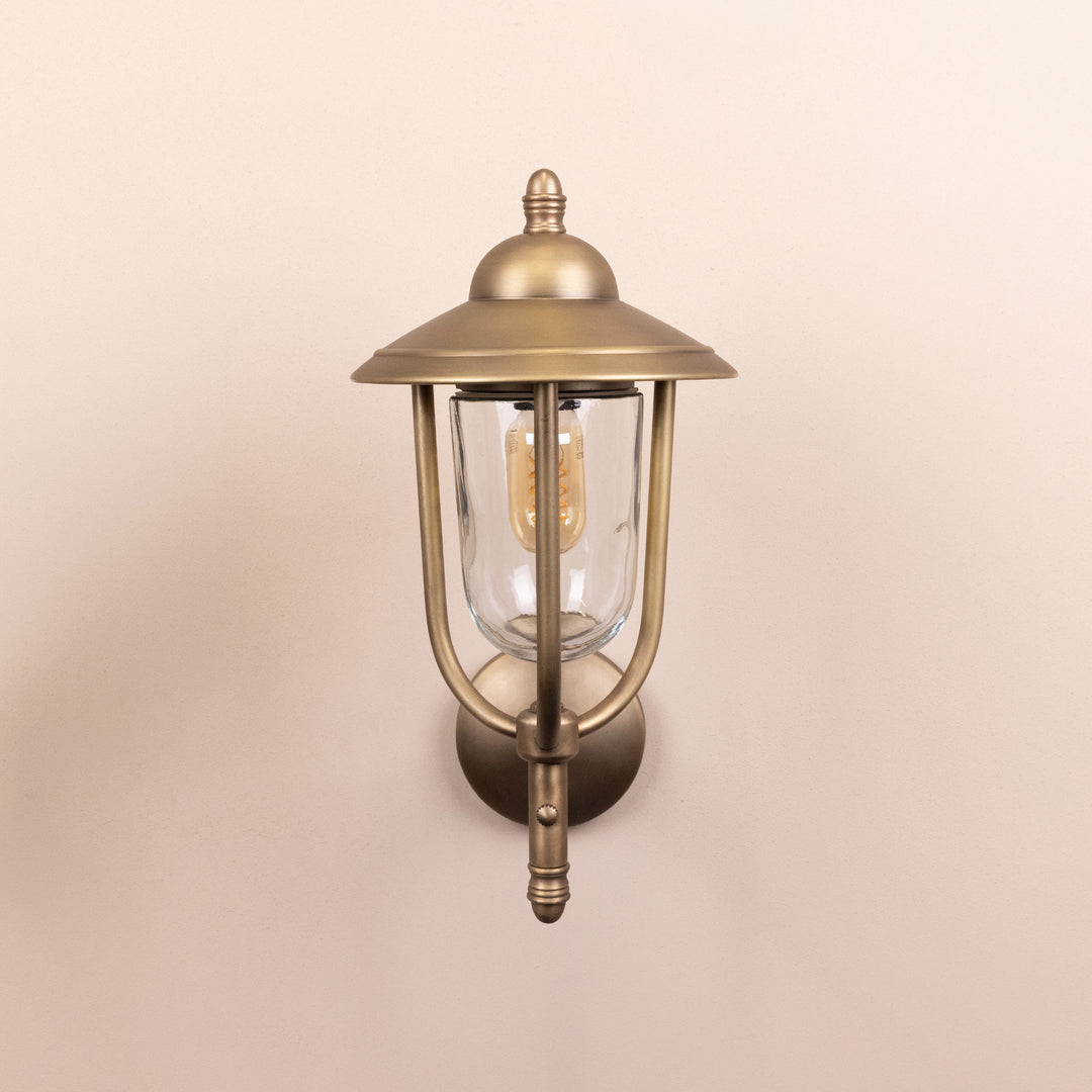 Front on image of the Agriframes Kensington Outdoor Wall Lamp in a Brass finish with its bulb switched off, mounted on a neutral background. 