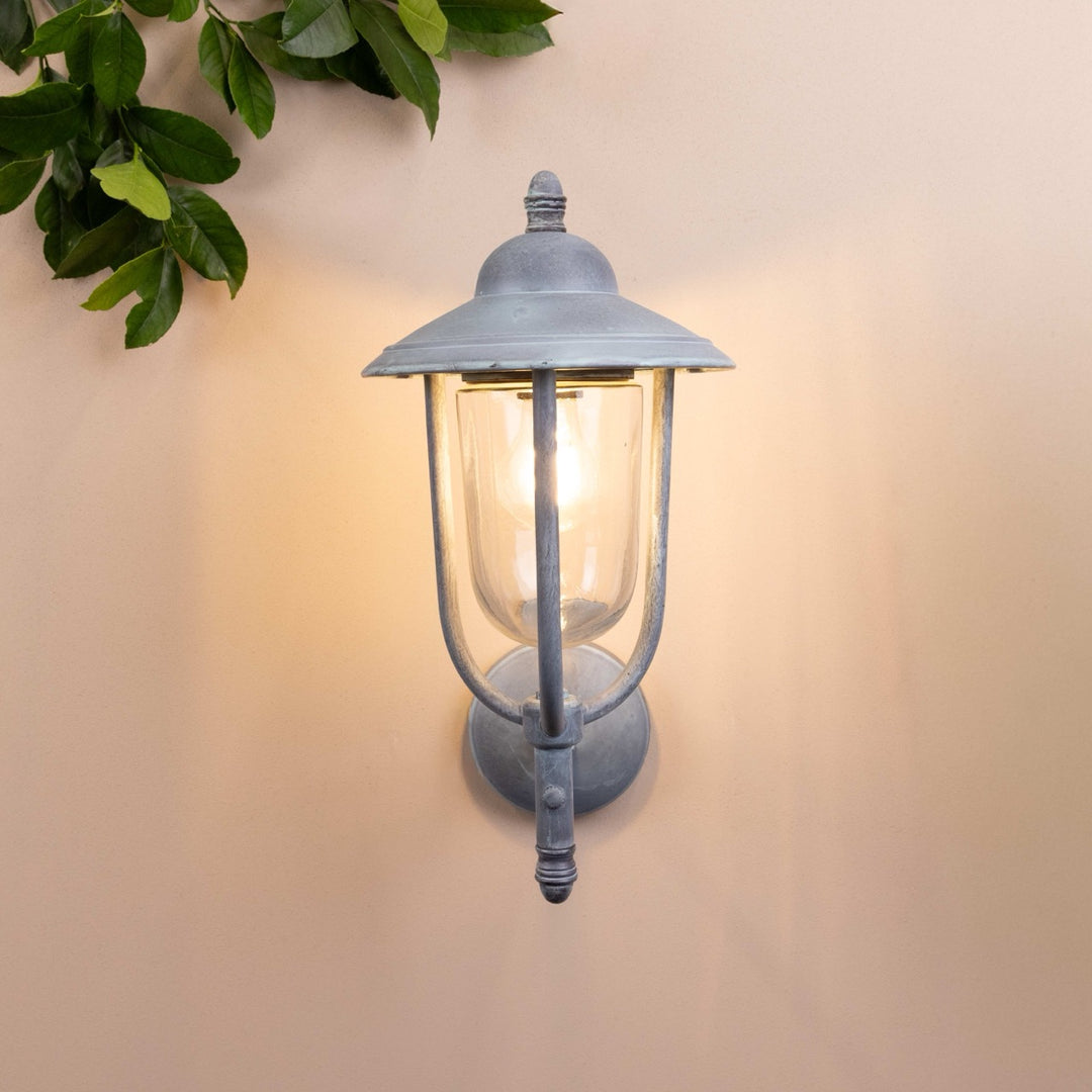 Front on image of the Agriframes Kensington Outdoor Wall Lamp in an Old Iron finish with its bulb illuminated, mounted on a neutral background. 