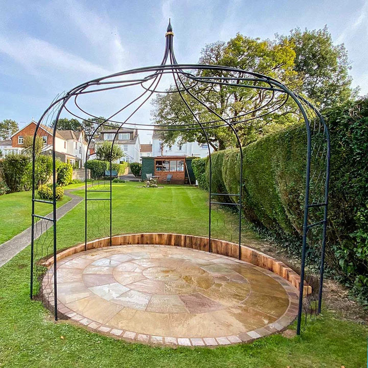 Metal pergola over a stone patio in a garden with houses in the background