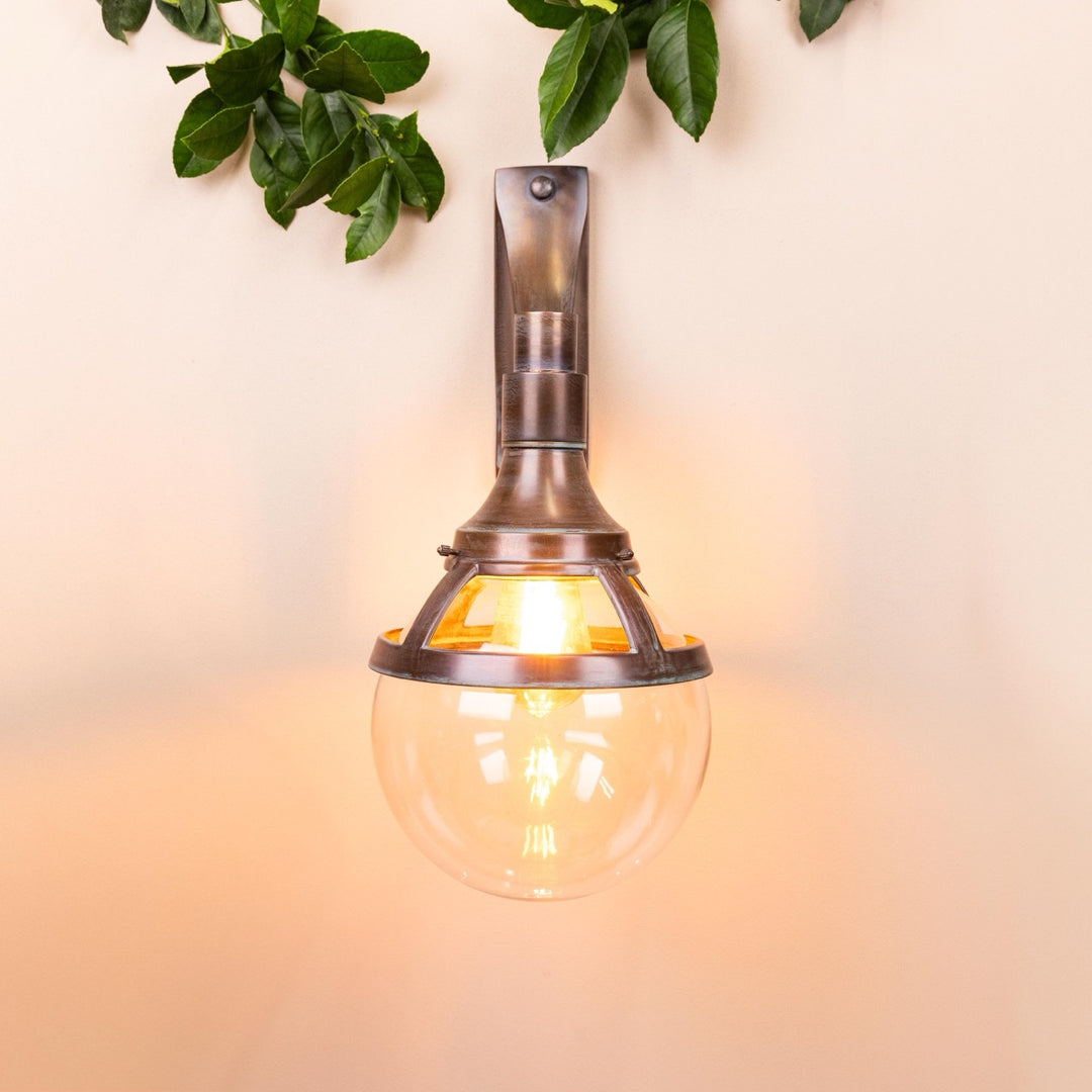 Front on image of the Agriframes London Outdoor Wall Lamp in a Copper finish with its bulb illuminated, mounted on a neutral background. 