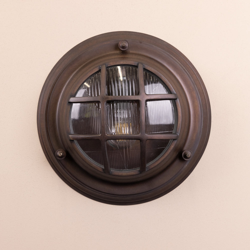 Front on image of the Agriframes Looe Bulk Head Round Lantern in a Bronze finish with its bulb switched off, mounted on a neutral background. 