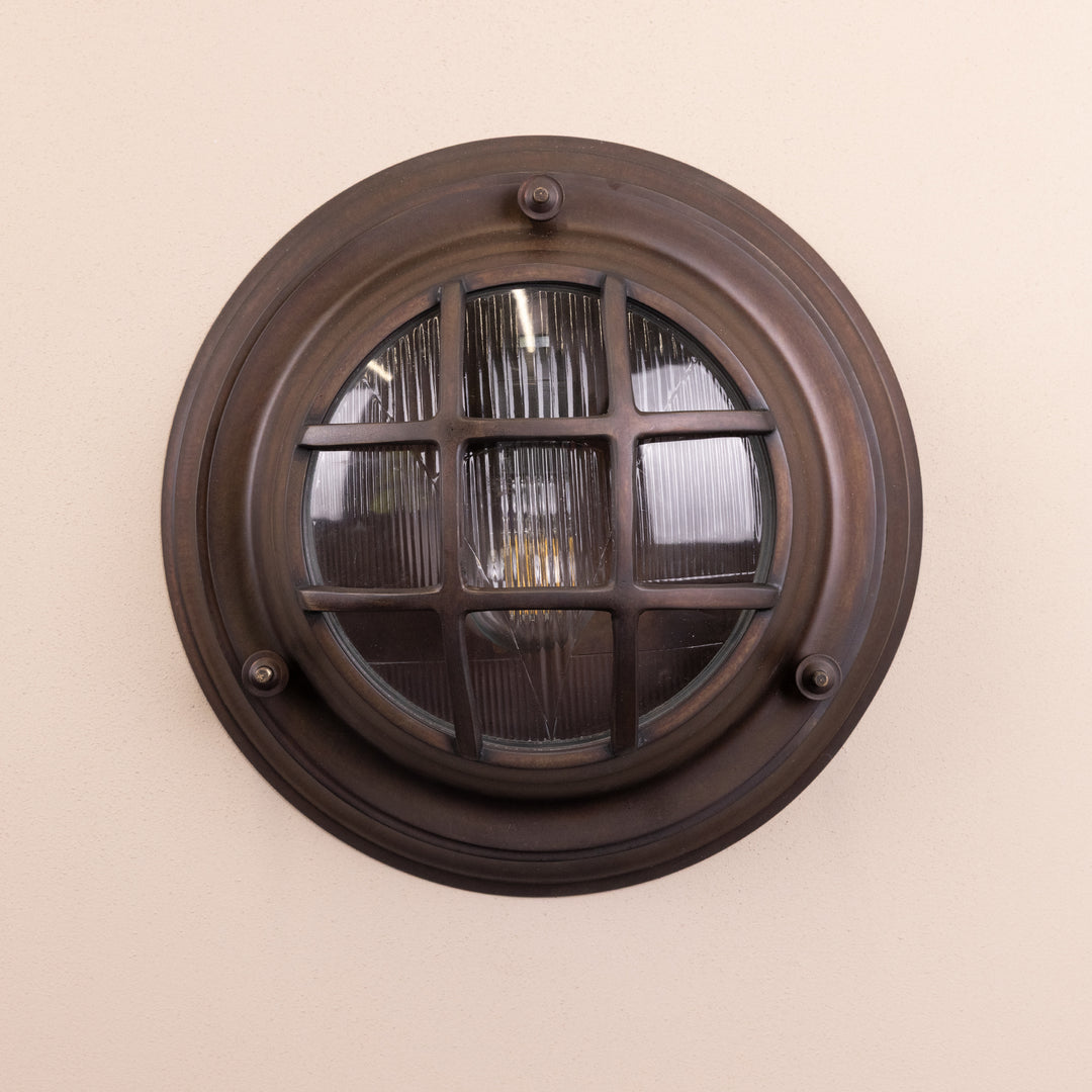 Front on image of the Agriframes Looe Bulk Head Round Lantern in a Bronze finish with its bulb switched off, mounted on a neutral background. 