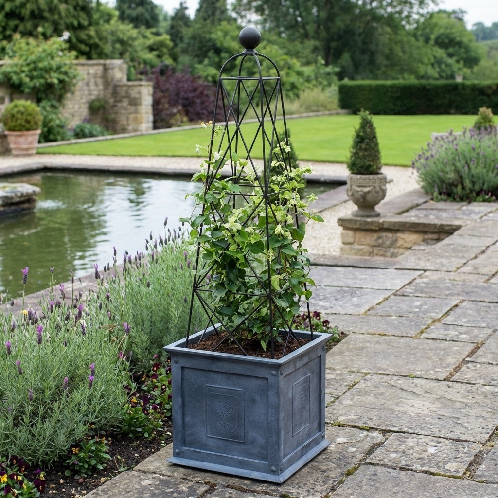 Decorative Agriframes RHS Zinc planter with climbing plant and King Obelisk in a garden setting with pond and stone pathway.