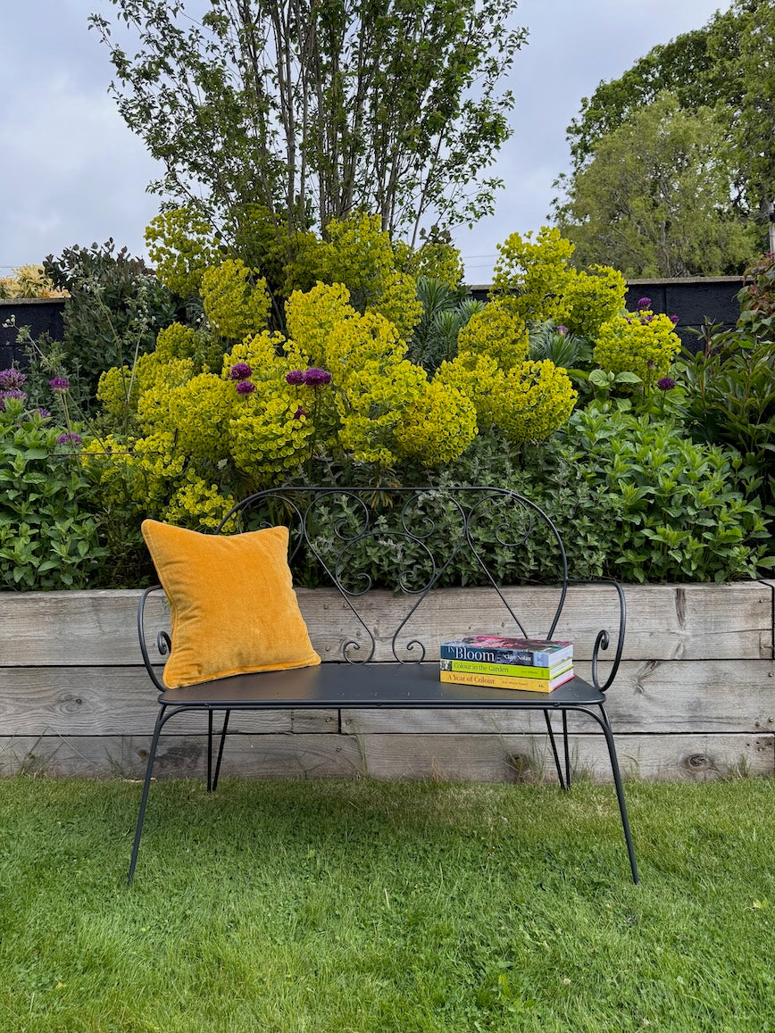 Pavillion Garden Bench on a lawn with a stack of books and a yellow cushion on the seat