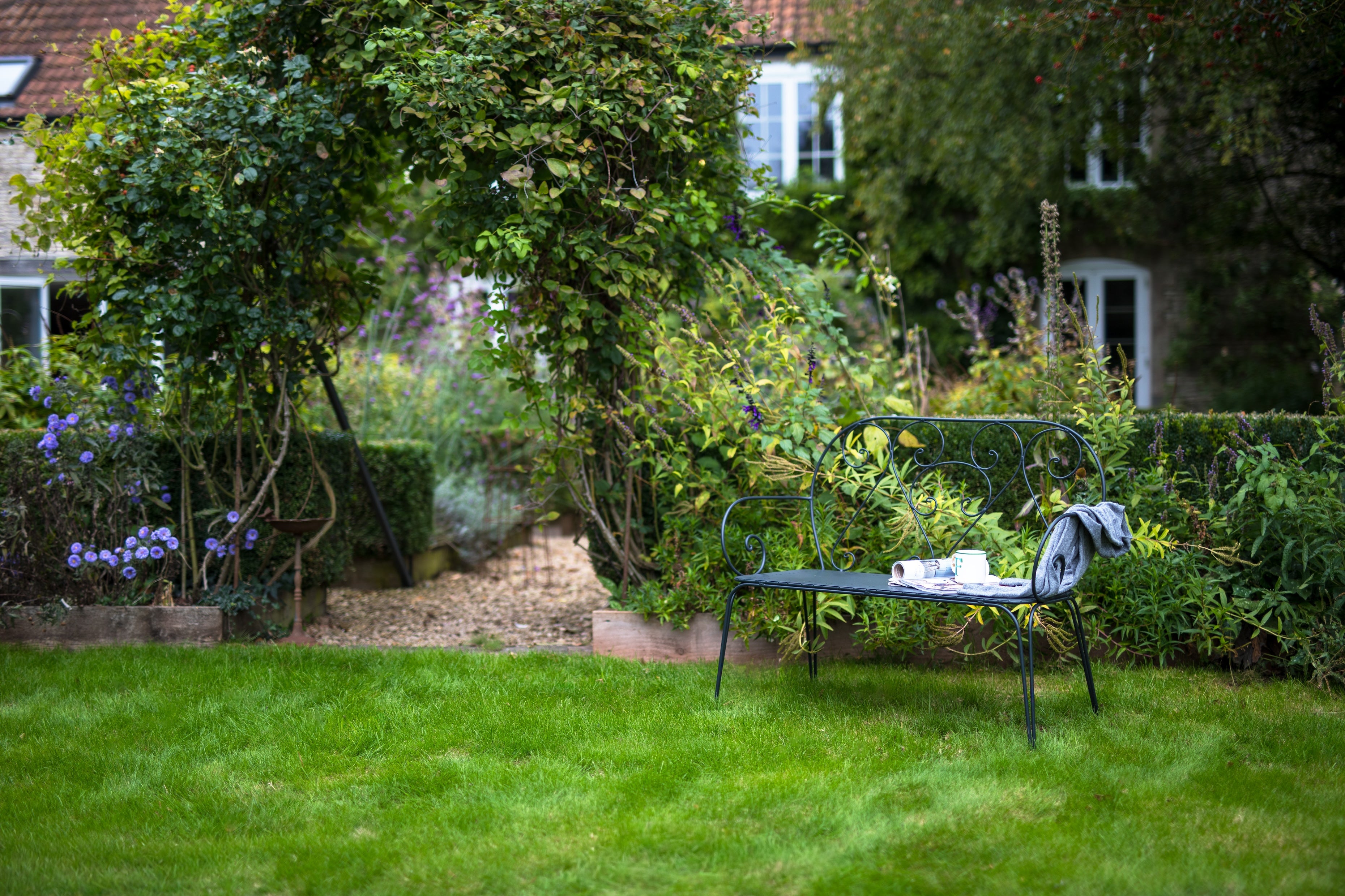 Agriframes Pavillion Vintage Garden Bench in a garden setting with a mug and magazines resting on the seat.