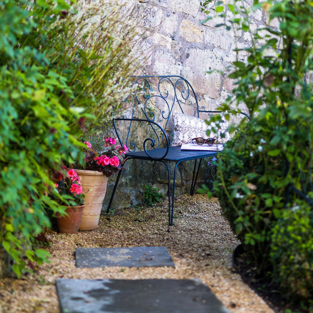Agriframes Pavillion Vintage Garden Bench in a garden setting with potted plants and a stone wall.