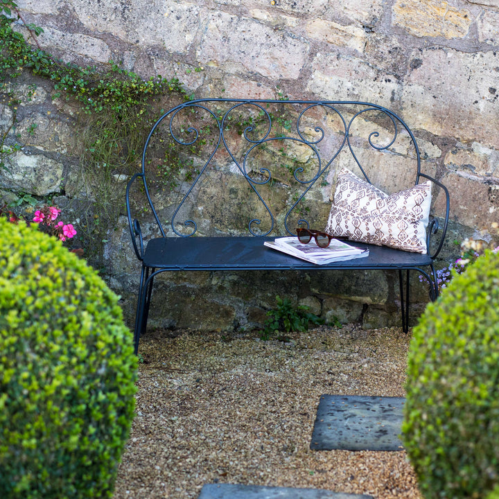 Decorative Agriframes Pavillion Vintage Garden Bench | metal bench with a cushion against a stone wall in a garden setting.