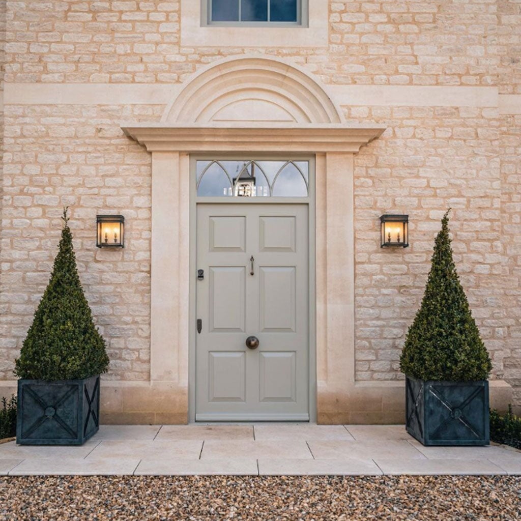 Gray front door of a house with stone walls and decorative plants on either side.