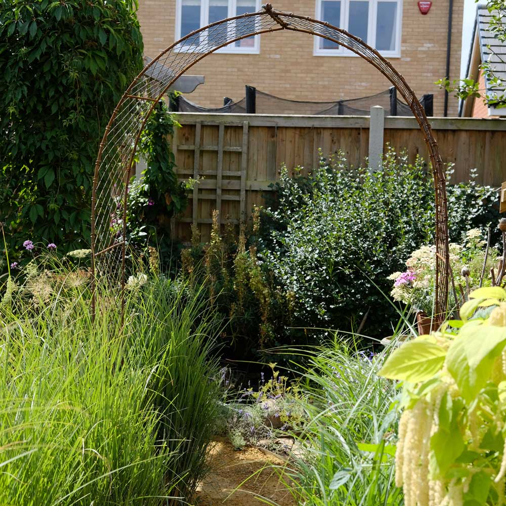 Elegance Round Arch in Rustic finish installed in a busy garden scene.