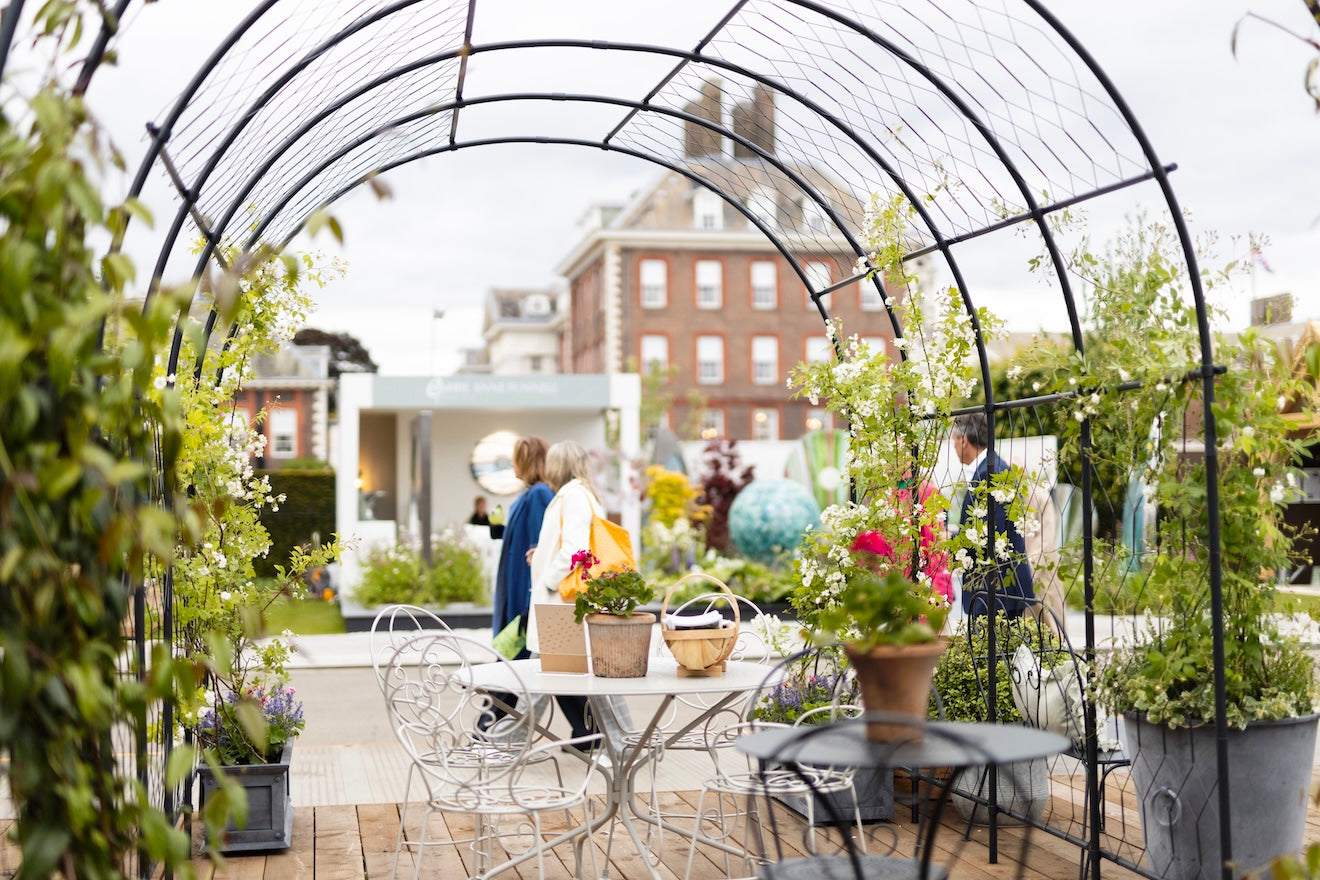 Agriframes Round Pergola with flowers growing up the frames and a table and chair set underneath at RHS chelsea flower show 2026.