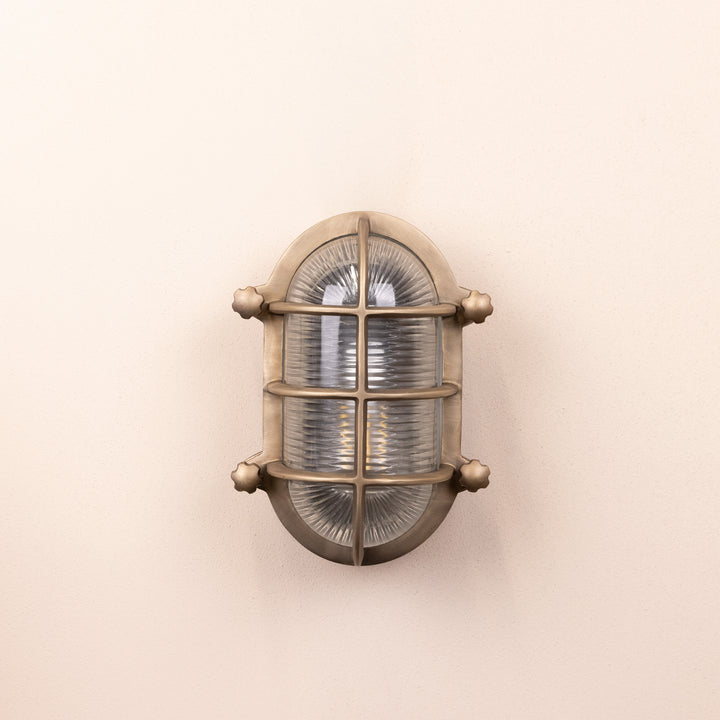 Front on image of the Agriframes Bulk Head Oval Lantern in a Brass finish with its bulb switched off, mounted on a neutral background. 