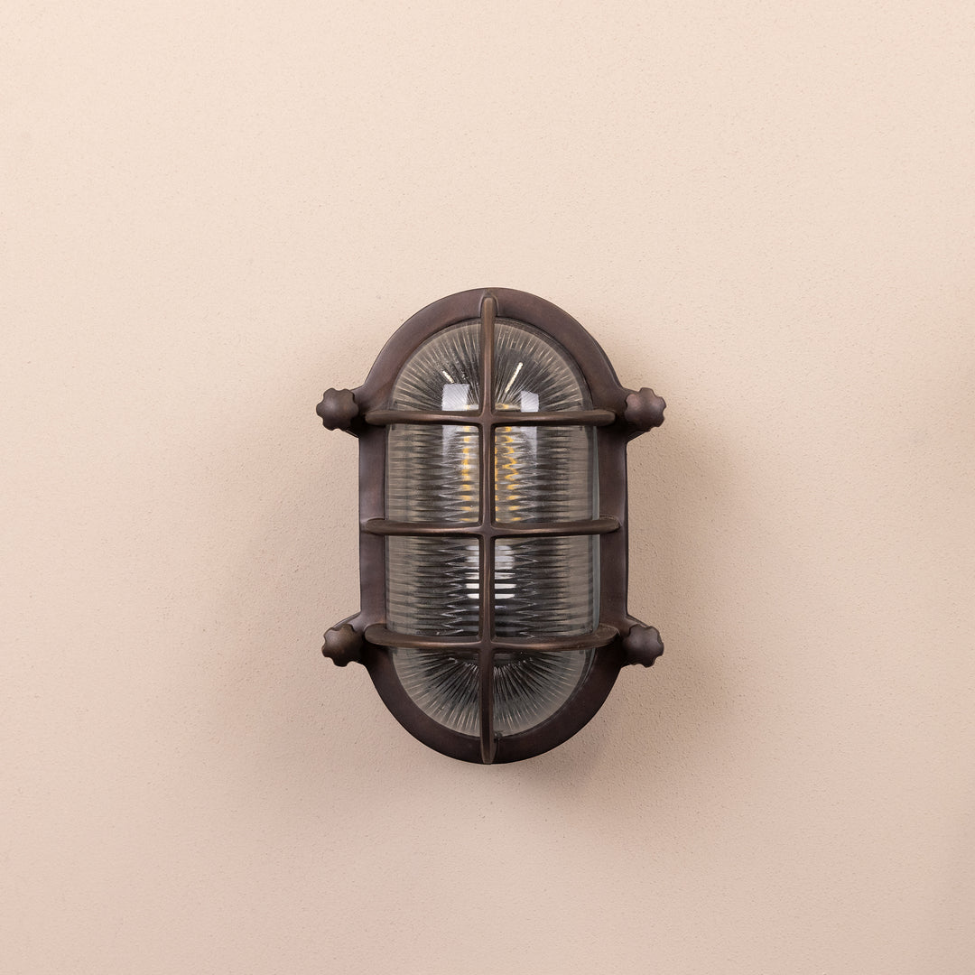 Front on image of the Agriframes Salcombe Bulk Head Oval Lantern in a Bronze finish with its bulb switched off, mounted on a neutral background. 