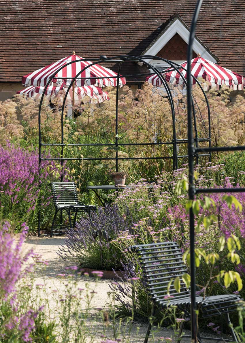 Agriframes round arbour with a table and chairs underneath in a large garden