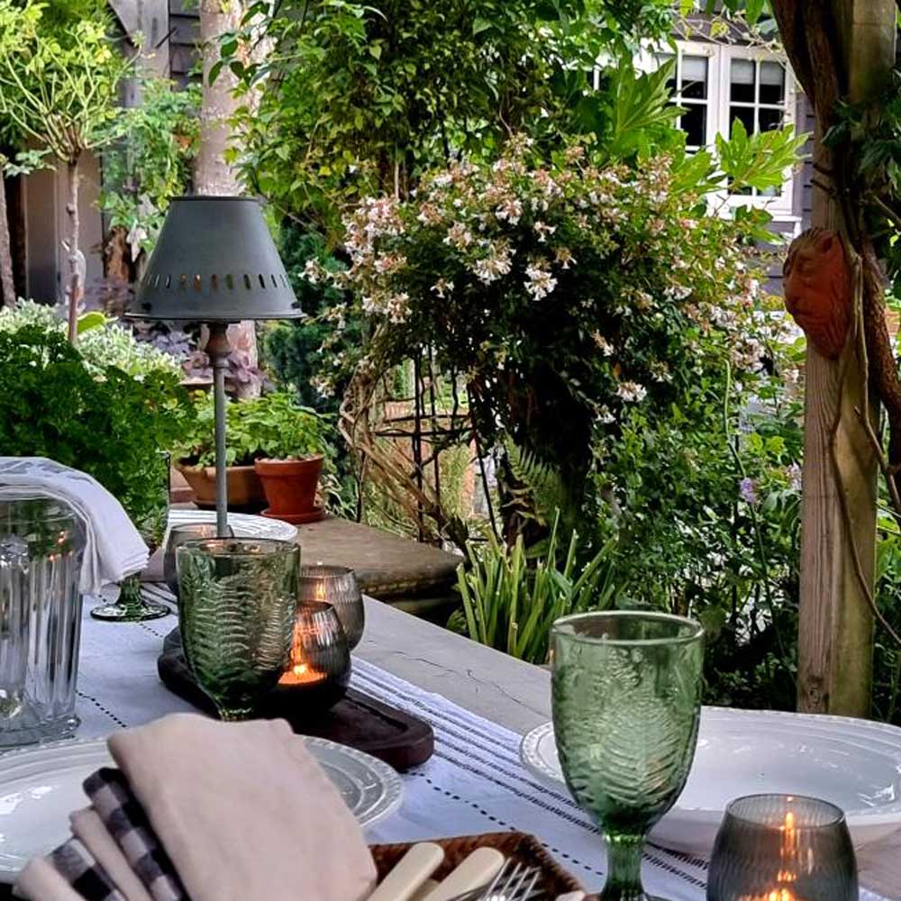 Outdoor dining setup with green glasses, candles, and a garden view.
