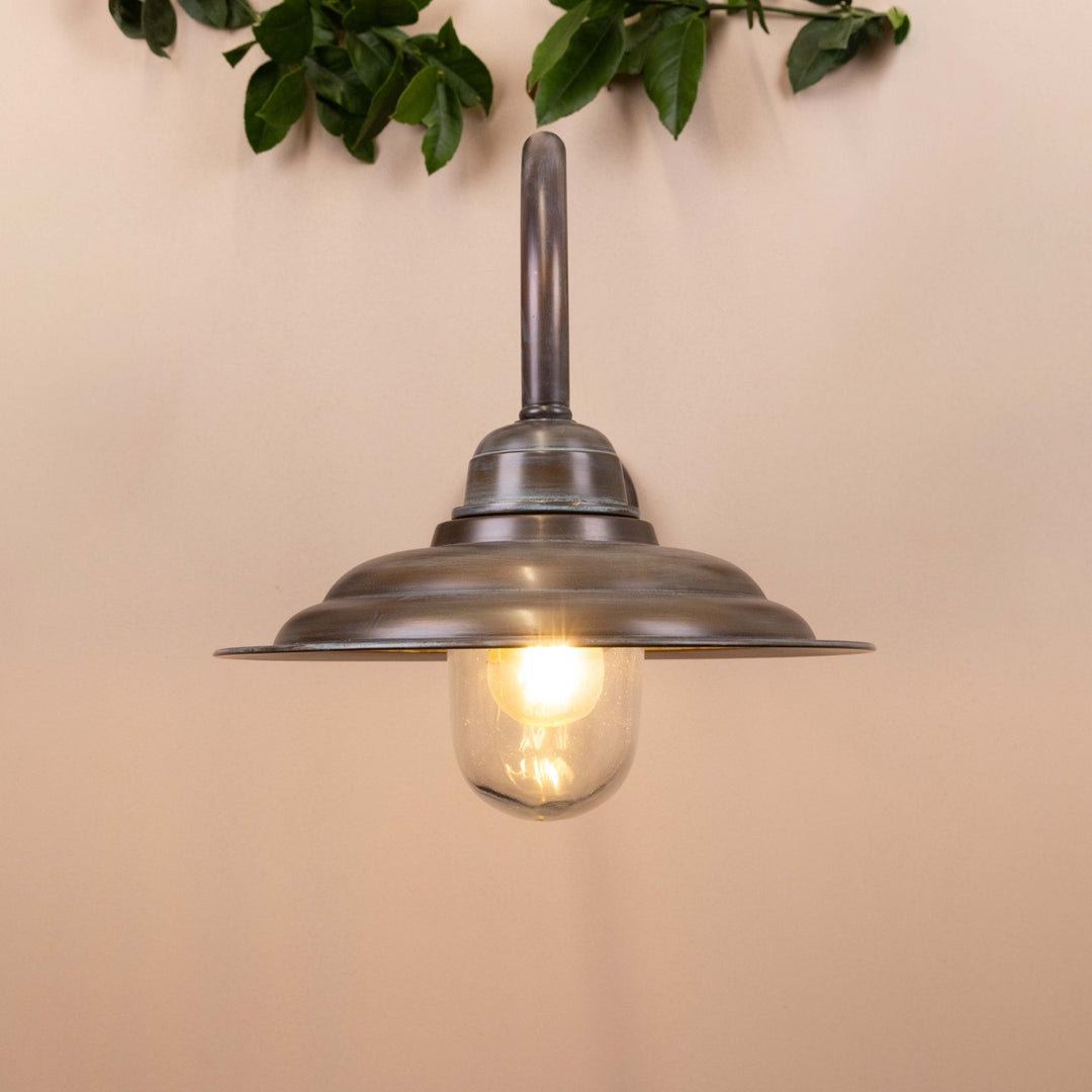 Copper patina wall-mounted lamp on a neutral background with leaves hanging above. 