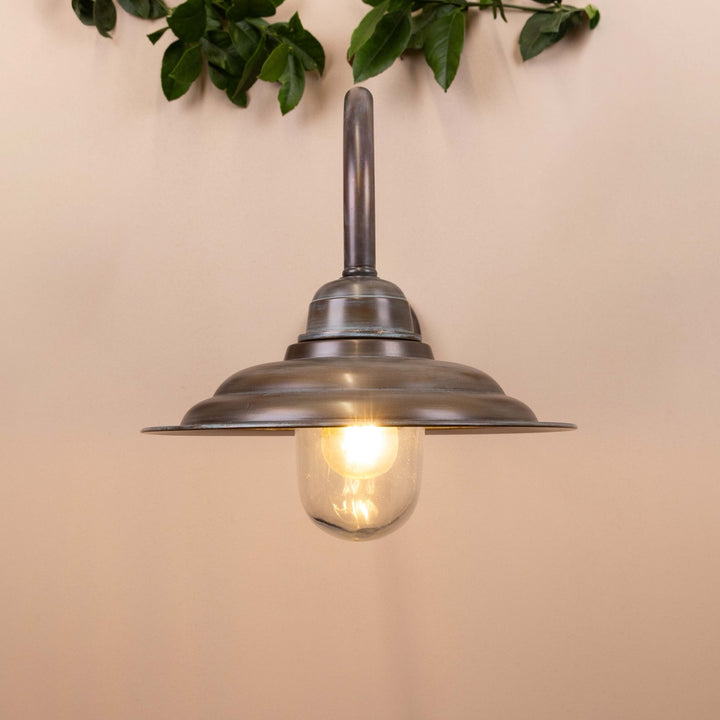 Copper patina wall-mounted lamp on a neutral background with leaves hanging above. 