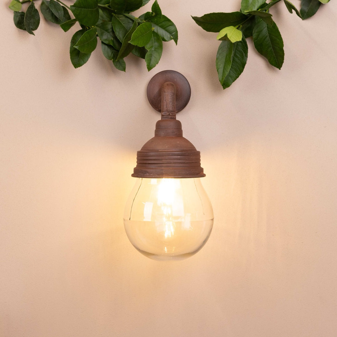 Rust-coloured wall lamp mounted on a beige background with decorative leaves hanging above.