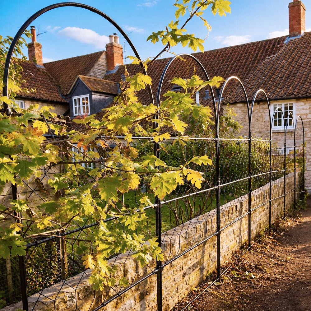 Several agriframes versatility screens linked together to make a fence against a short wall on the border of a soil bed, with a plant climbing up the frame