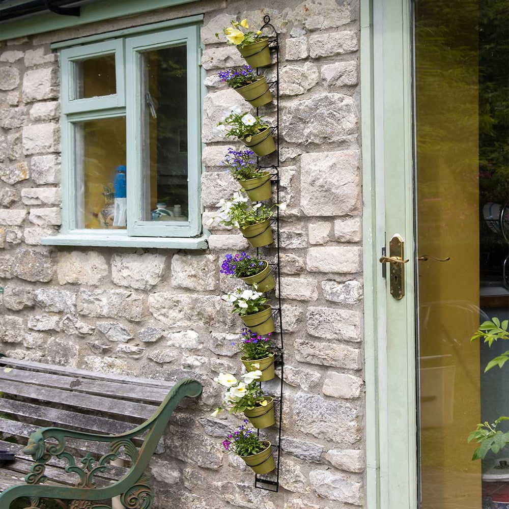 Vertical plant holder with potted plants on a stone wall next to a window.