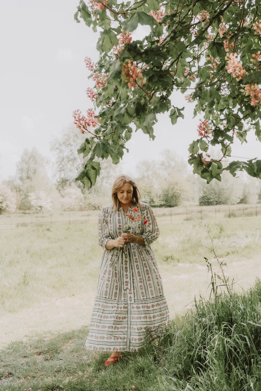 Woman in a long dress in a field holdibng a bunch of flowers