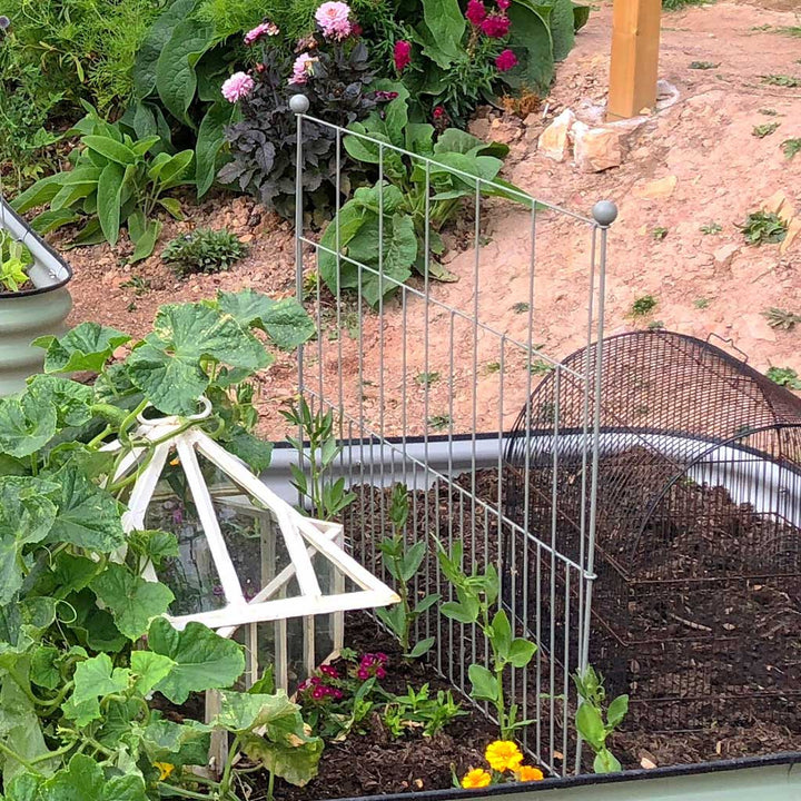 Agriframes Deco Panel Plant Support in Sage Green installed in a flowerbed with various plants growing next to it. 